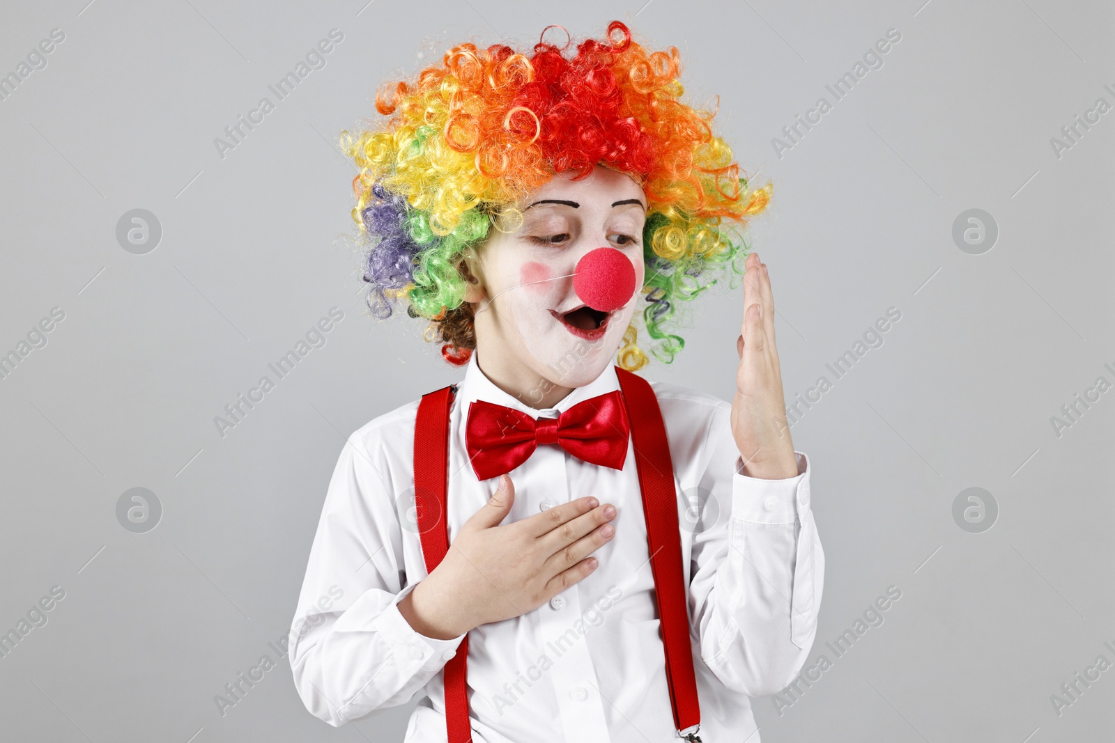 Photo of Cute little boy in clown wig and red nose on grey background. Surprise party