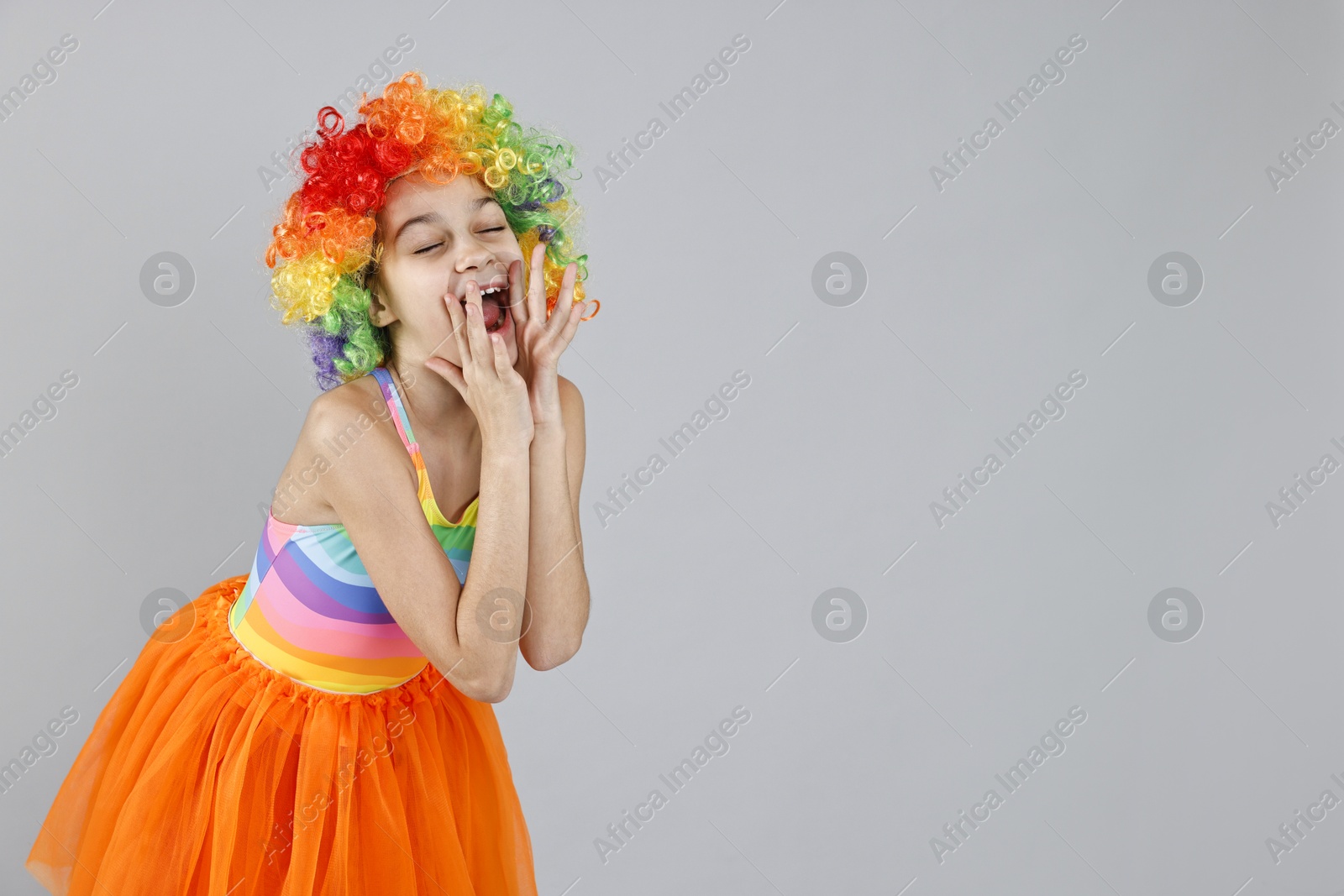 Photo of Cute girl dressed like clown shouting on grey background, space for text. Surprise party