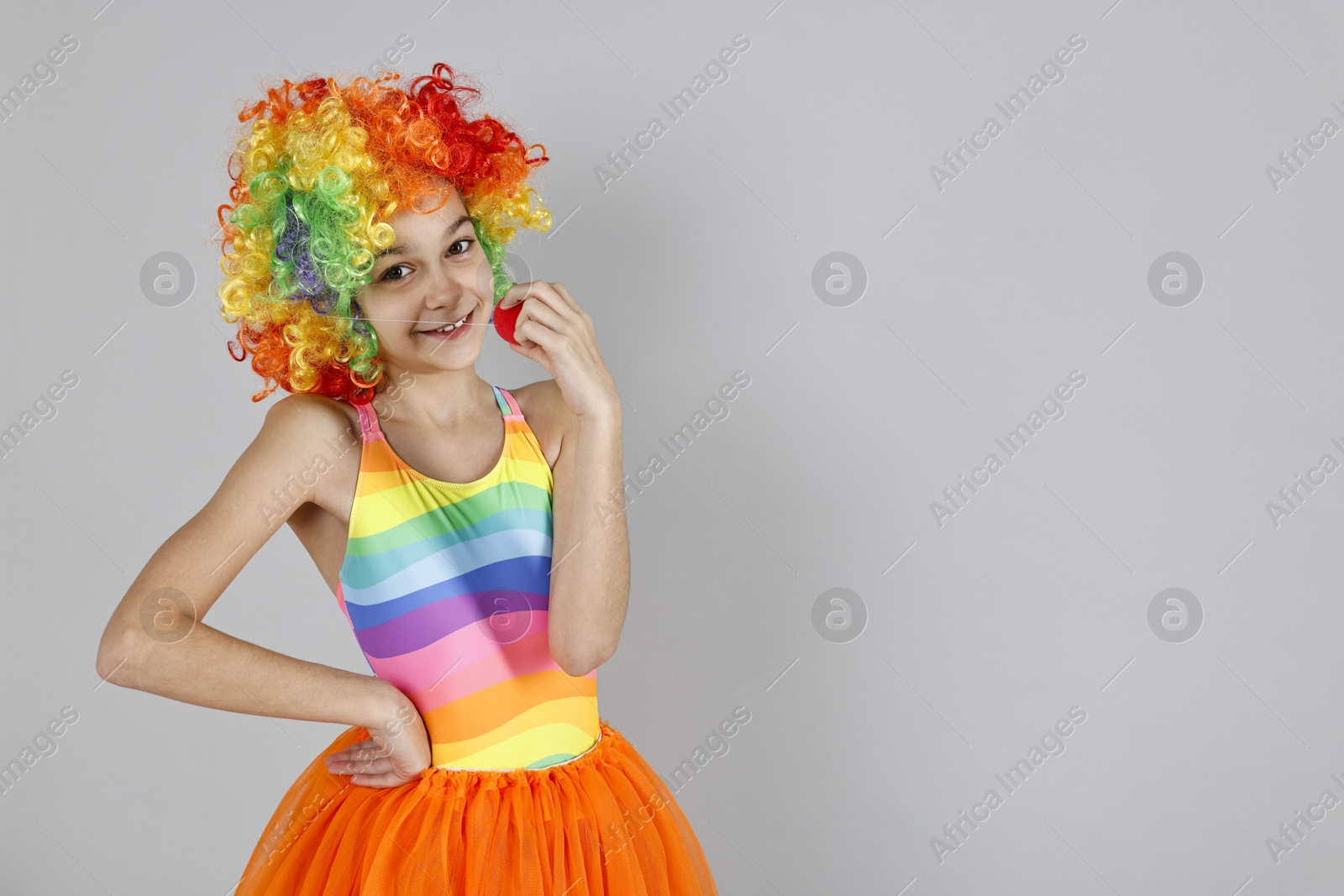 Photo of Happy girl dressed like clown on grey background, space for text. Surprise party