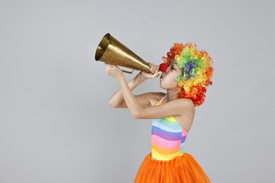 Photo of Girl dressed like clown with megaphone on grey background, space for text. Surprise party