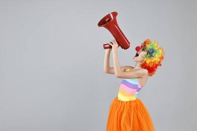 Photo of Girl dressed like clown shouting in megaphone on grey background, space for text. Surprise party