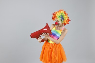 Photo of Happy girl dressed like clown with megaphone on grey background, space for text. Surprise party