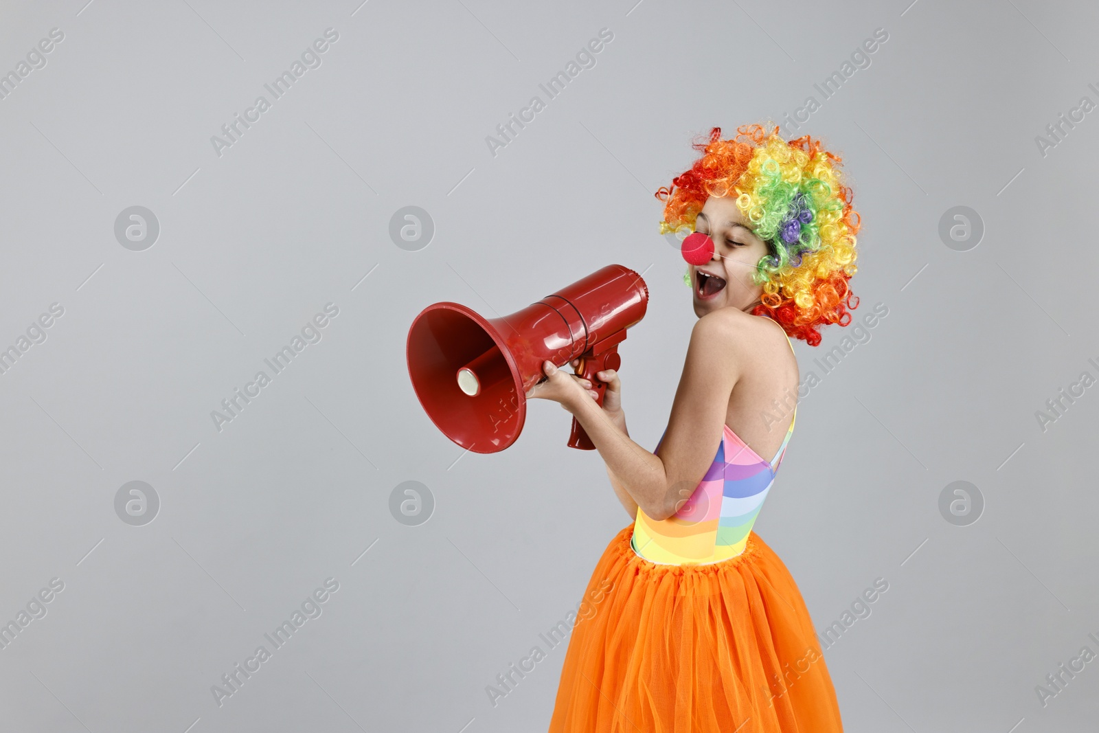 Photo of Girl dressed like clown with megaphone on grey background, space for text. Surprise party