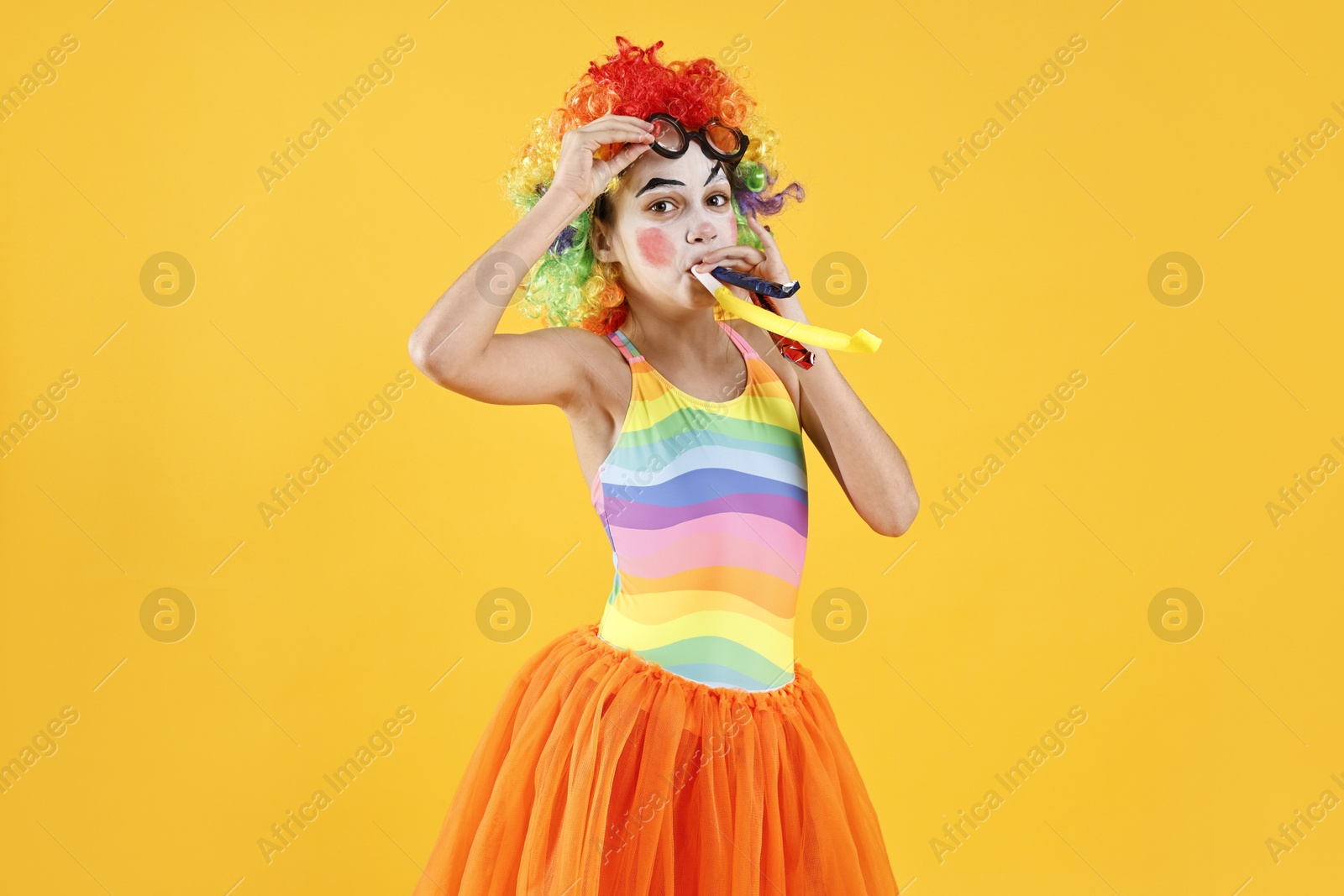 Photo of Girl dressed like clown with blowers on yellow background. Surprise party