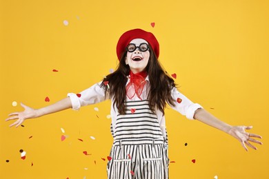 Photo of Happy girl dressed like mime under falling confetti on yellow background. Surprise party