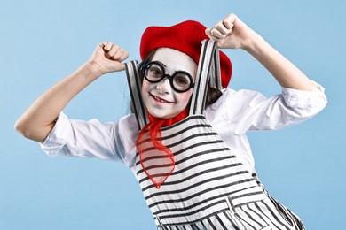 Photo of Happy girl dressed like mime on light blue background. Surprise party