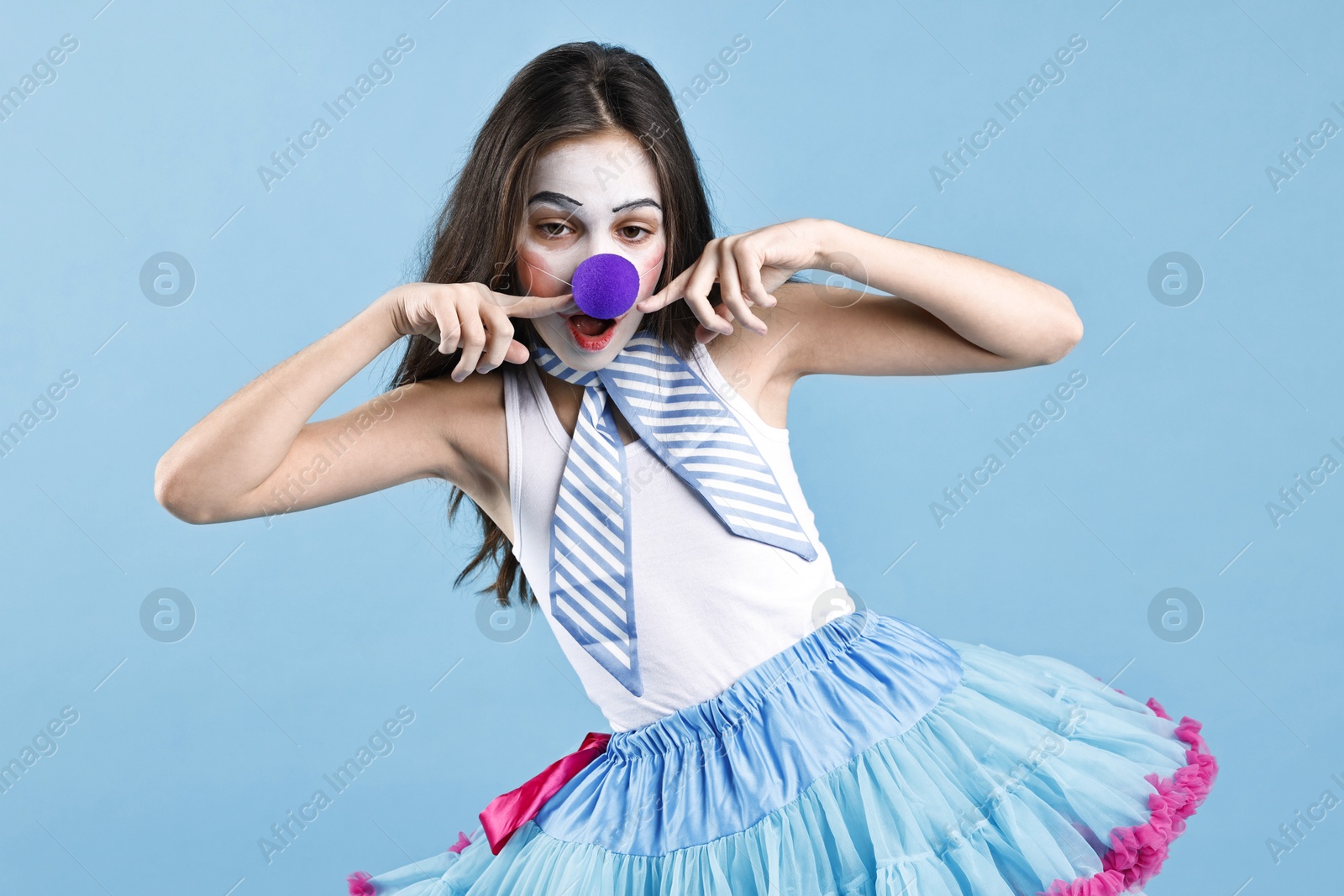 Photo of Cute girl dressed like clown on light blue background. Surprise party