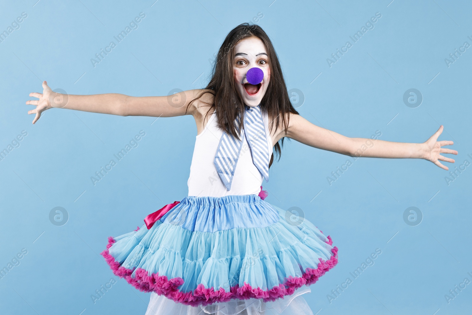 Photo of Happy girl dressed like clown with wide open arms on light blue background. Surprise party