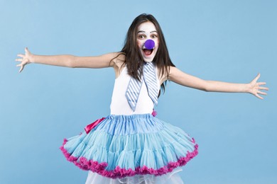 Photo of Happy girl dressed like clown with wide open arms on light blue background. Surprise party