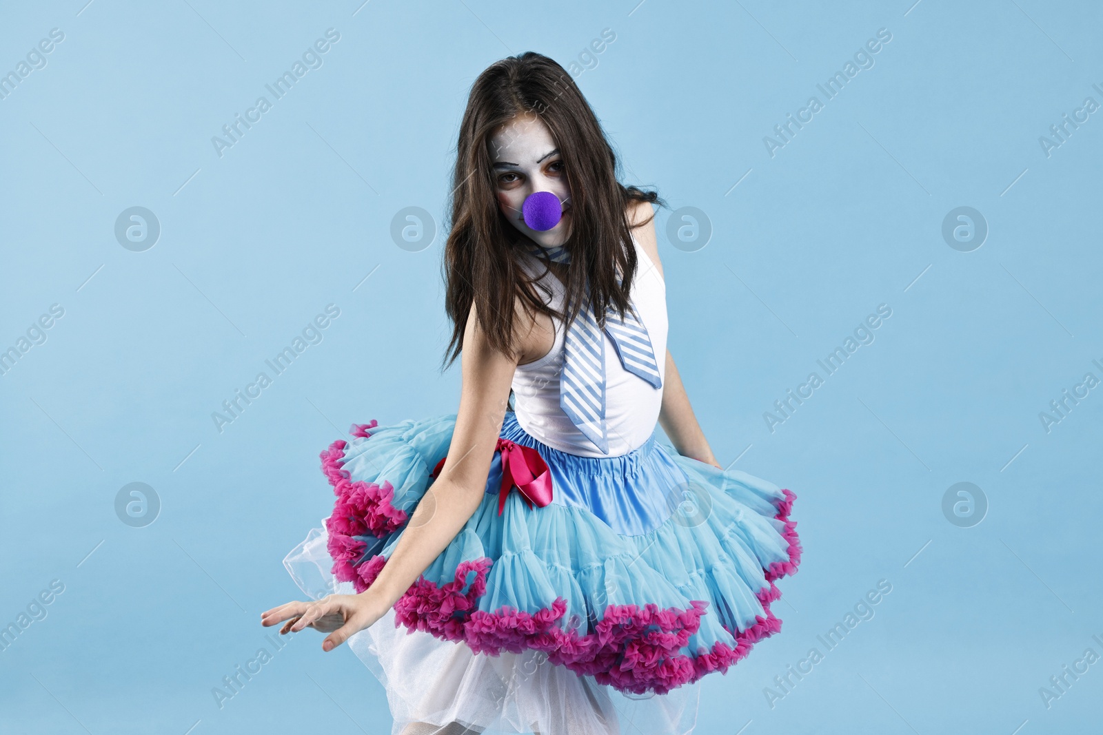 Photo of Cute girl dressed like clown on light blue background. Surprise party