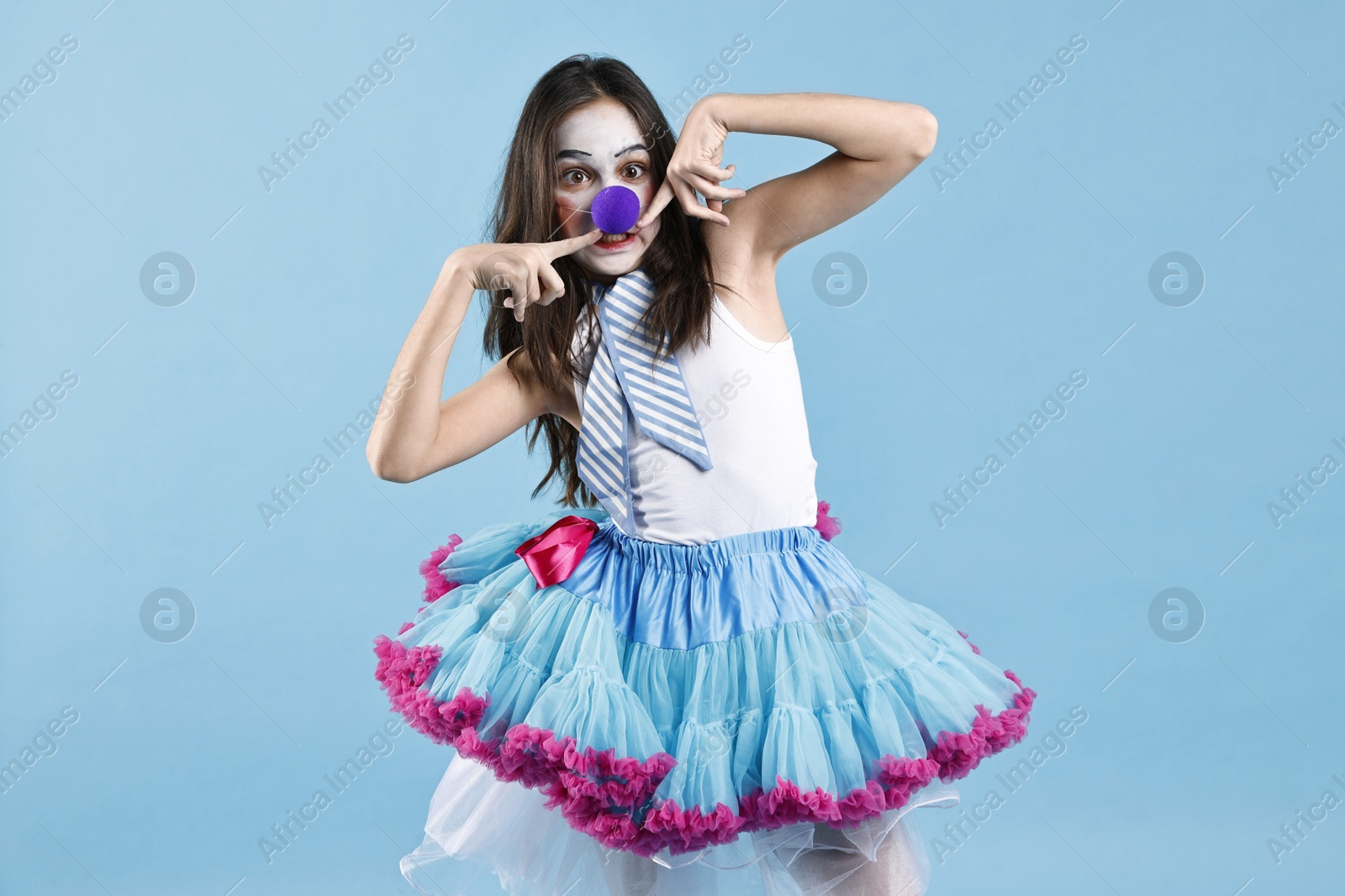 Photo of Cute girl dressed like clown on light blue background. Surprise party