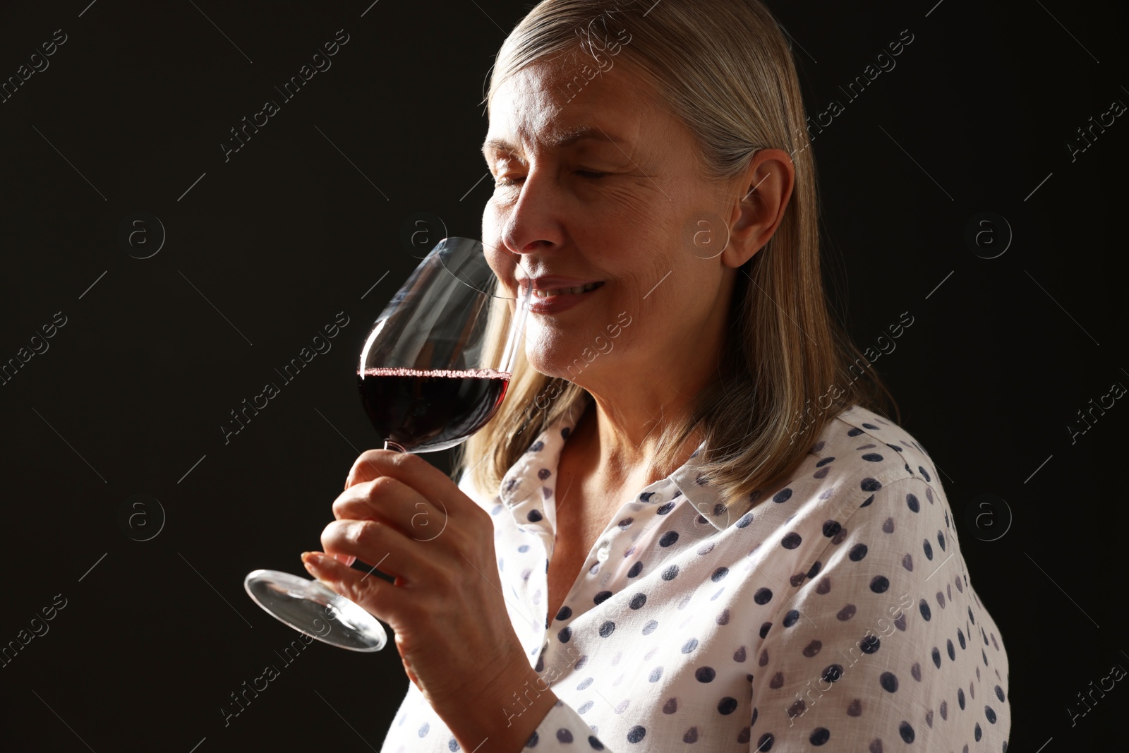 Photo of Professional sommelier tasting red wine in glass on black background