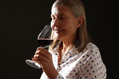 Photo of Professional sommelier tasting red wine in glass on black background