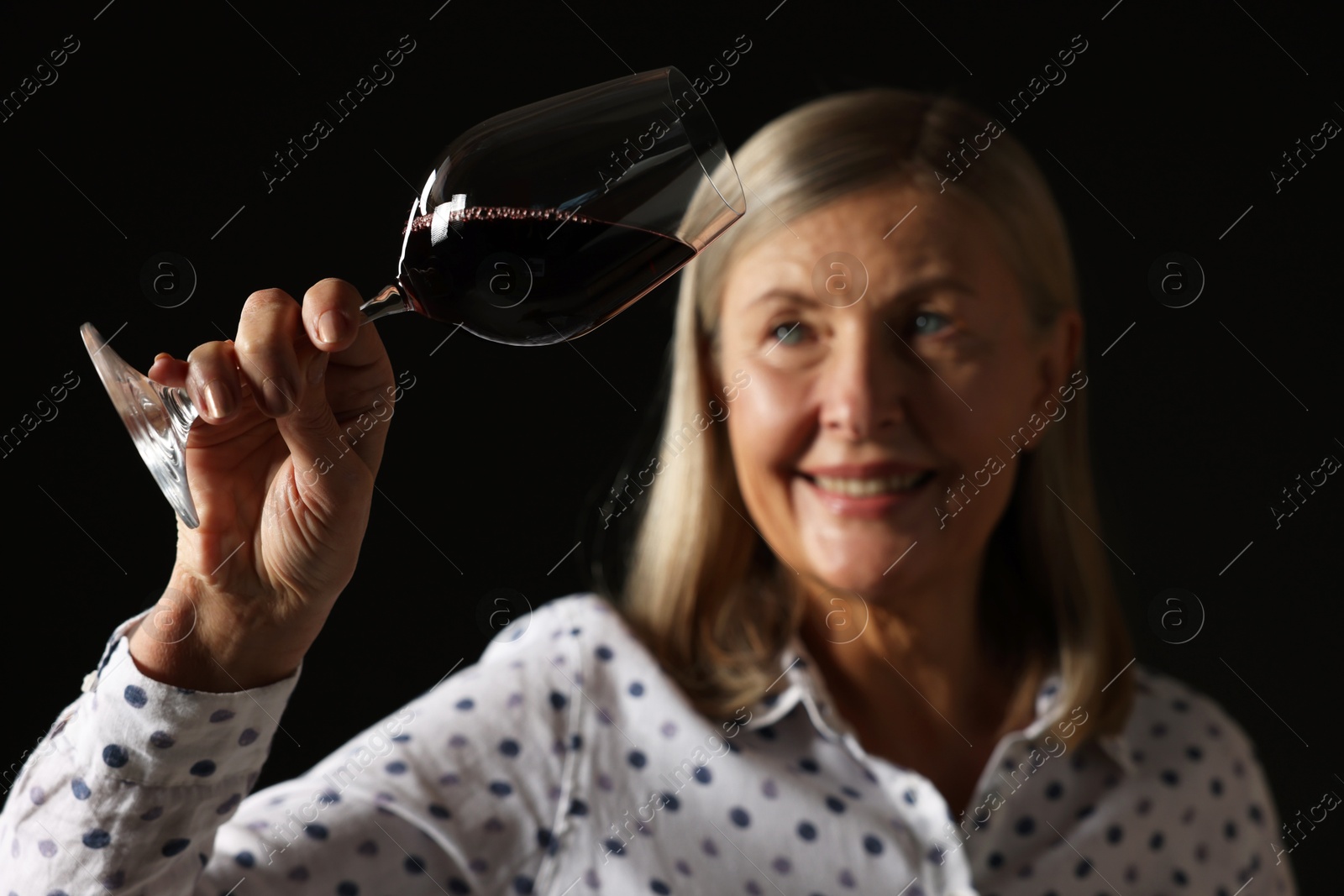 Photo of Professional sommelier analyzing quality of red wine on black background, selective focus