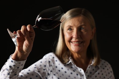 Photo of Professional sommelier analyzing quality of red wine on black background, selective focus