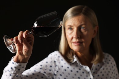 Photo of Professional sommelier analyzing quality of red wine on black background, selective focus