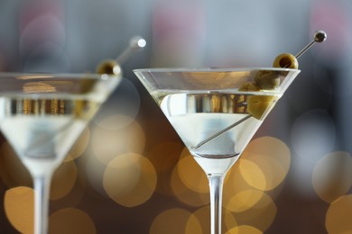 Photo of Martini cocktail with olives in glasses on blurred background, closeup. Bokeh effect