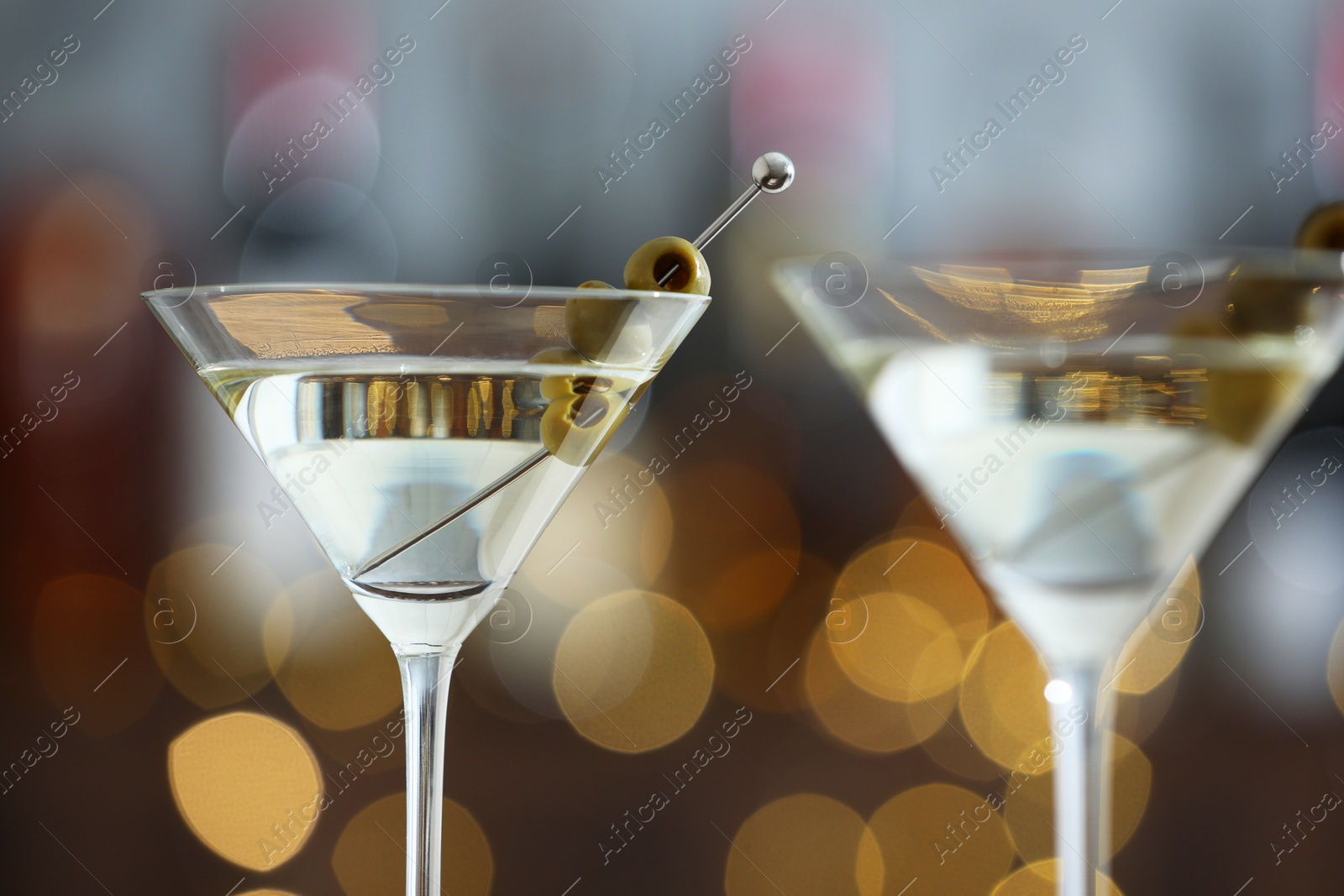 Photo of Martini cocktail with olives in glasses on blurred background, closeup. Bokeh effect