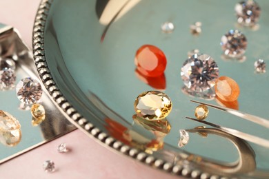 Photo of Tray with beautiful gemstones and tweezers on light pink table, closeup