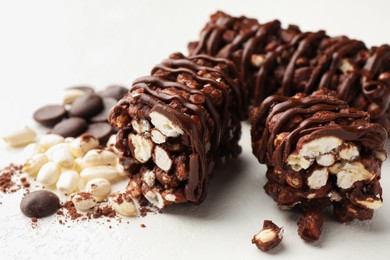 Photo of Delicious chocolate puffed rice bars and cacao chips on white table, closeup