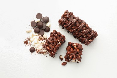 Photo of Delicious chocolate puffed rice bars and cacao chips on white table, flat lay