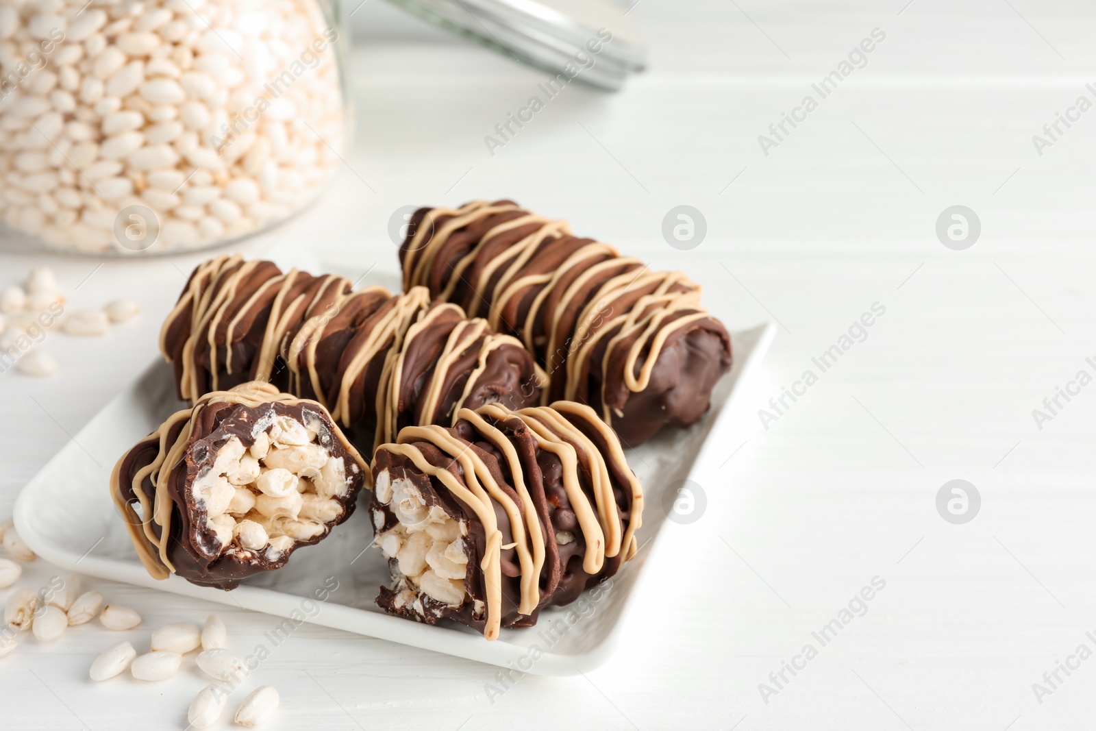 Photo of Delicious chocolate puffed rice bars on white wooden table, closeup. Space for text