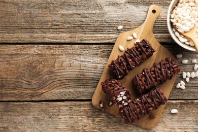 Photo of Delicious chocolate puffed rice bars on wooden table, flat lay. Space for text