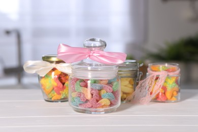 Photo of Tasty gummy candies in jars on light wooden table indoors