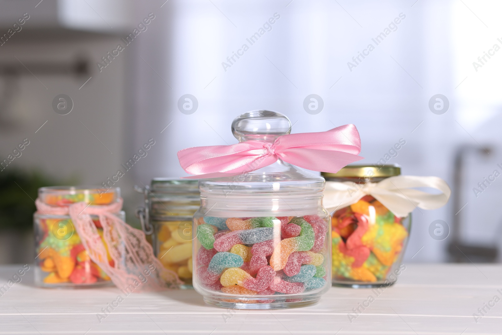 Photo of Tasty gummy candies in jars on light wooden table indoors