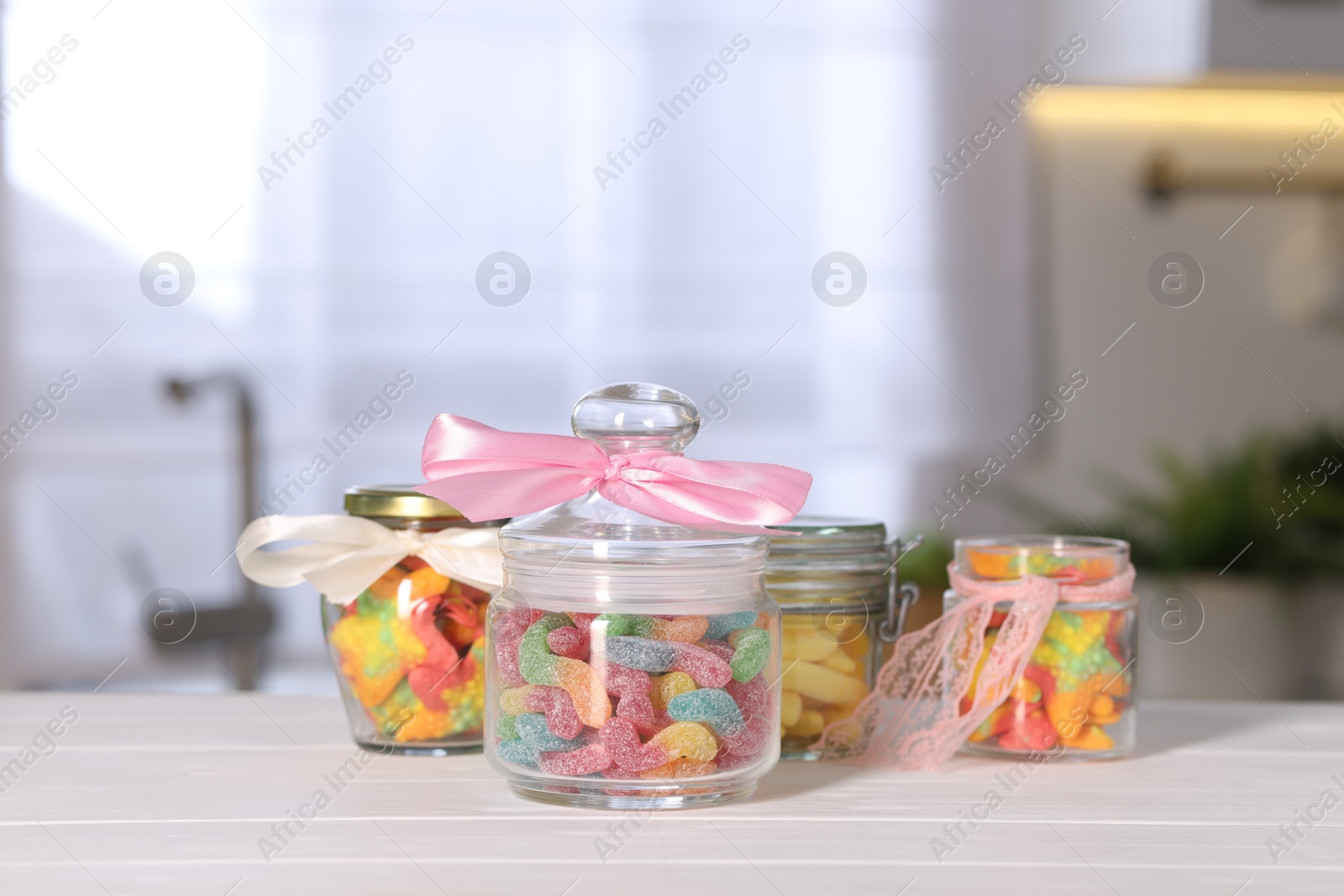 Photo of Tasty gummy candies in jars on light wooden table indoors