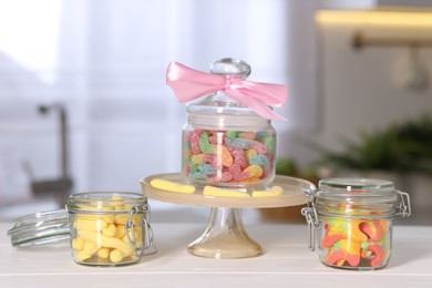 Photo of Tasty gummy candies in jars on light wooden table indoors