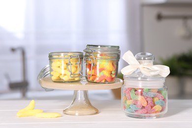 Photo of Tasty gummy candies in jars on light wooden table indoors