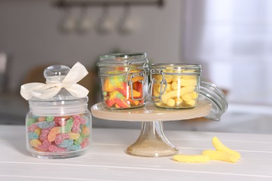 Photo of Tasty gummy candies in jars on light wooden table indoors