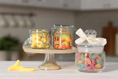 Photo of Tasty gummy candies in jars on light wooden table indoors