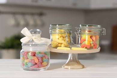 Photo of Tasty gummy candies in jars on light wooden table indoors