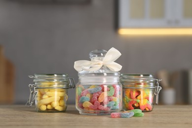 Photo of Tasty gummy candies in jars on wooden table indoors