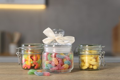 Photo of Tasty gummy candies in jars on wooden table indoors