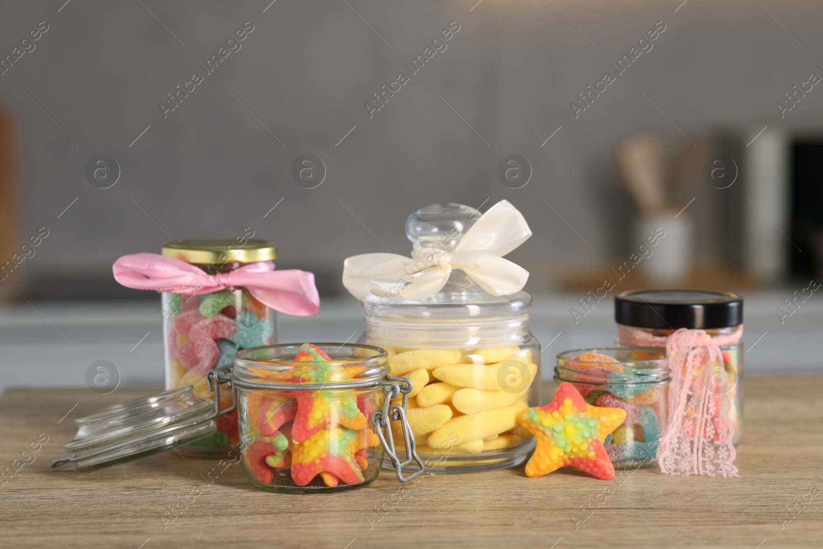 Photo of Tasty gummy candies in jars on wooden table indoors