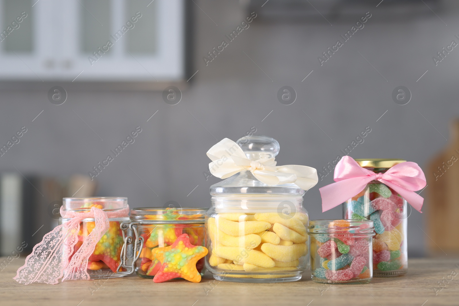 Photo of Tasty gummy candies in jars on wooden table indoors