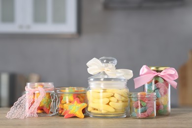 Photo of Tasty gummy candies in jars on wooden table indoors