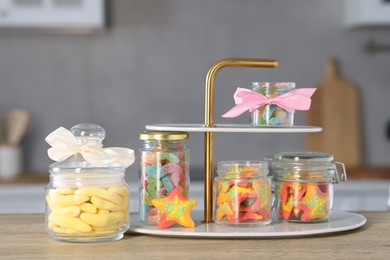 Photo of Tasty gummy candies in jars on wooden table indoors