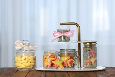 Photo of Tasty gummy candies in jars on wooden table indoors