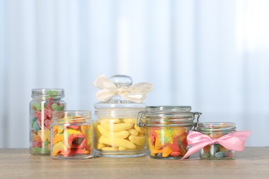 Photo of Tasty gummy candies in jars on wooden table indoors