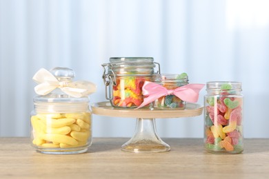 Photo of Tasty gummy candies in jars on wooden table indoors