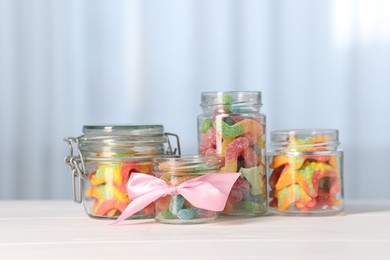 Photo of Tasty gummy candies in jars on light wooden table indoors