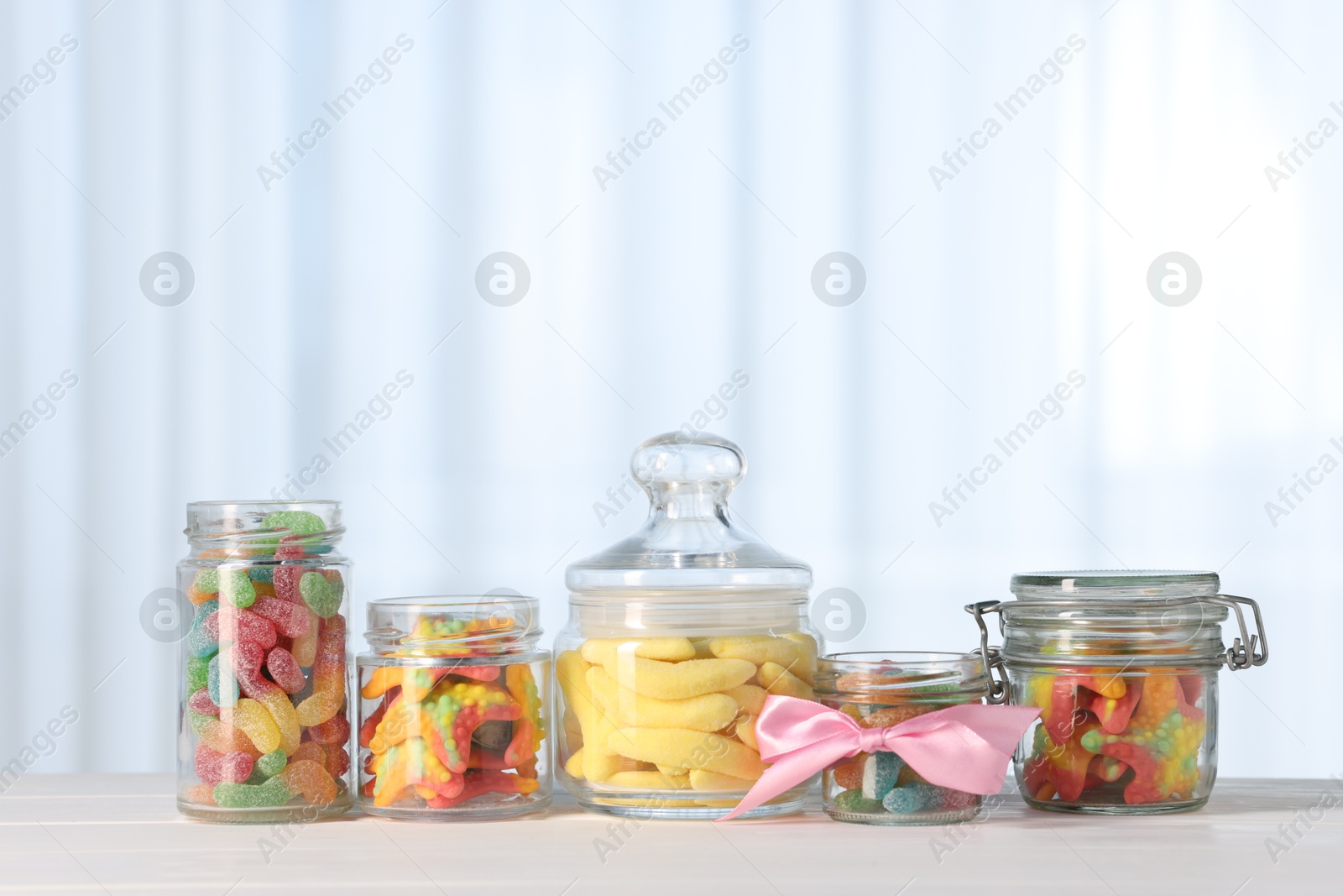 Photo of Tasty gummy candies in jars on light wooden table indoors