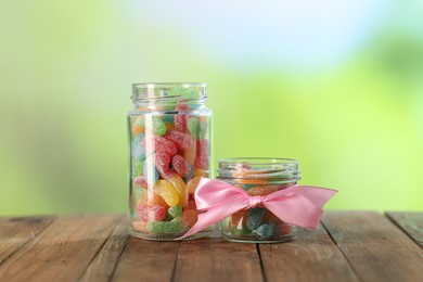 Photo of Tasty gummy candies in jars on wooden table against blurred green background