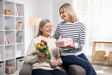 Photo of Smiling daughter congratulating her mom with bouquet of tulips and gift at home. Happy Mother's Day