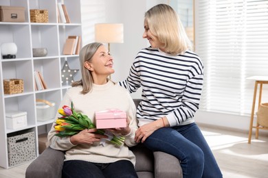 Photo of Smiling daughter congratulating her mom with bouquet of tulips and gift at home. Happy Mother's Day