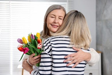 Photo of Smiling mom receiving bouquet of tulips from her daughter at home. Happy Mother's Day